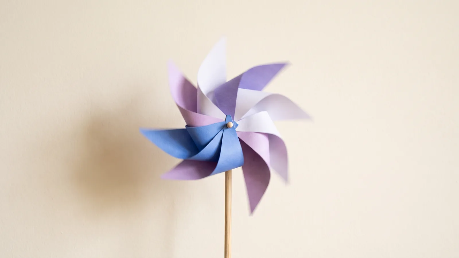 A blue and violet paper pinwheel spins in front of a pale cream wall.